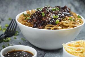 Teriyaki Grilled Chicken Noodles with green onion, spicy sauce, cabbage salad and fork served in bowl isolated on grey background closeup side view of chinese food photo