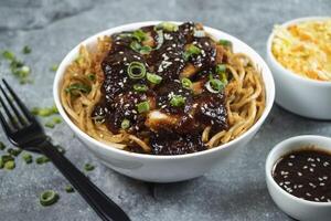 Teriyaki Fried Chicken Noodles with green onion, spicy sauce, cabbage salad and fork served in bowl isolated on grey background closeup side view of asian food photo