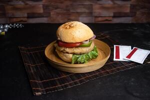 Classic Chicken Burger include tomato, onion, lettuce leave, capsicum and sauce served in wooden plate isolated on dark background side view of bangladeshi fast food photo