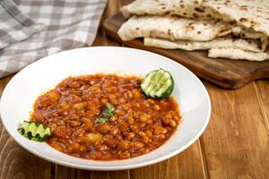 Spicy Red beans with pita bread served in plate isolate on wooden table side view of arabic food photo