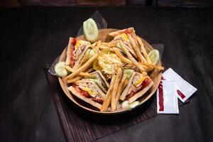 ultimate club sandwich with french fries and sauce served in basket isolated on dark background side view of bangladeshi fast food photo