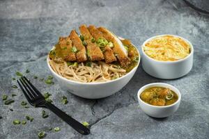 Katsu Chicken Noodles with potato curry, cabbage salad, green onion and fork served in bowl isolated on grey background side view of asian food photo