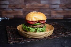 Classic Beef Burger include tomato, onion, lettuce leave and capsicum served in wooden plate isolated on dark background side view of bangladeshi fast food photo