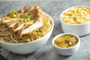 Katsu Chicken Noodles with potato curry, cabbage salad, green onion and fork served in bowl isolated on grey background closeup side view of japan food photo