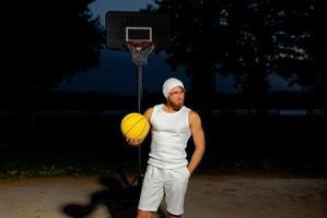 Man holding a basketball in a park at dusk, showcasing athleticism and confidence by the court under a darkening sky photo