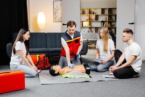 Young man instructor helping to make first aid heart compressions with dummy during the group training indoors photo