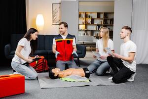 Young man instructor helping to make first aid heart compressions with dummy during the group training indoors photo