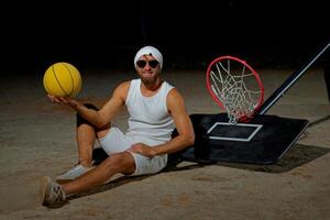 A basketball player sits on the court wearing sunglasses, relaxed after an intense practice session at dusk photo