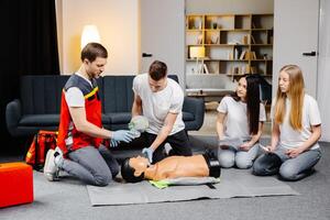 Young man instructor helping to make first aid heart compressions with dummy during the group training indoors photo