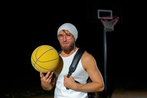 A man prepares for a night basketball game with a yellow ball at an outdoor court under dim lighting photo