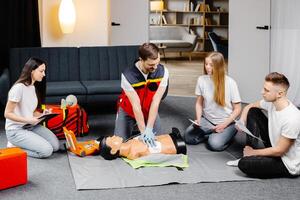 Young man instructor helping to make first aid heart compressions with dummy during the group training indoors photo