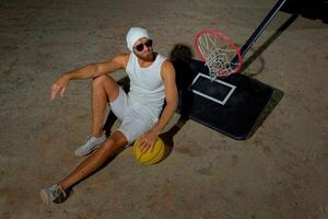 A basketball player sits on the court wearing sunglasses, relaxed after an intense practice session at dusk photo