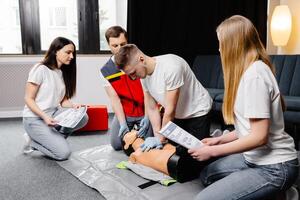 Young man instructor helping to make first aid heart compressions with dummy during the group training indoors photo
