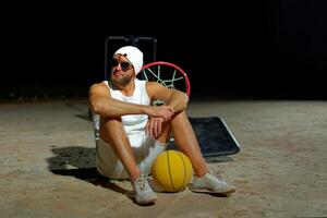 A basketball player sits on the court wearing sunglasses, relaxed after an intense practice session at dusk photo