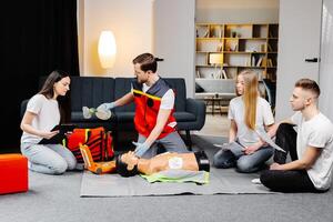 Young man instructor helping to make first aid heart compressions with dummy during the group training indoors photo