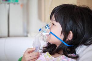 Sick little asian girl inhalation with nebulizer for respiratory treatment photo