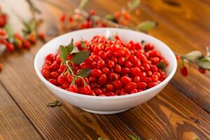 fresh ripe red goji berries in a bowl on a wooden table photo