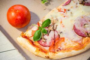 cooked pizza with salami and sausage in a box on a wooden table.On a wooden table photo