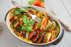 prepared baked zucchini and tomatoes in circles in a ceramic form. On a wooden table photo
