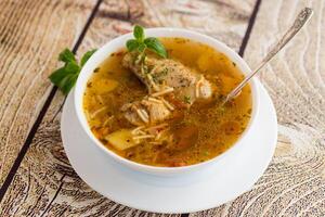 hot cooked chicken and noodle soup in a plate on a wooden table photo