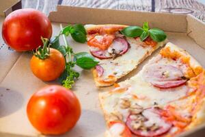 cooked pizza with salami and sausage in a box .On a wooden table photo