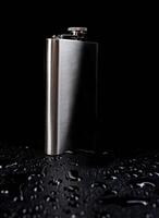 Flat stainless steel flask on a black background with water drops. photo