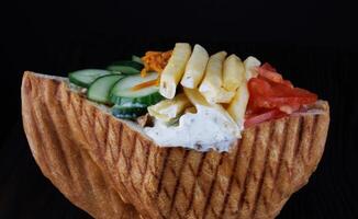Doner with a crispy crust and delicious meat and vegetable filling on a dark background. photo