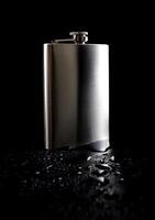 Flat stainless steel flask on a black background with water drops. photo