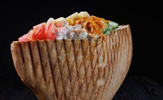 Doner with a crispy crust and delicious meat and vegetable filling on a dark background. photo