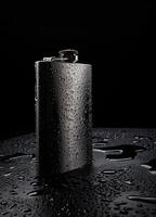 Stainless steel flask on a black background with water drops.Personal flat flask. photo