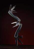 Steel open multitool on red background. Multitool with many useful tools. photo