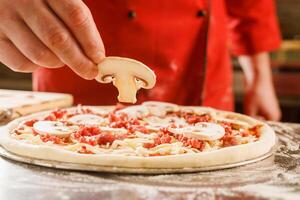 Chef adding mushrooms to uncooked pizza photo