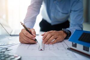 A man is drawing a house on a piece of paper with a pen. He is using a ruler to make sure the lines are straight. Concept of precision and attention to detail, as the man carefully draws the house photo