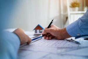 A man is drawing a house with a ruler and a pen. The house is small and has a blue roof. The man is focused on his drawing, and the scene conveys a sense of precision and attention to detail photo