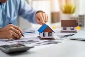 A man is drawing a house on a piece of paper. He is using a pen and a calculator photo