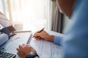 A man is writing on a piece of paper with a pen. He is sitting at a desk with a laptop and a calculator. The man is focused on his work, possibly working on a project or a report photo