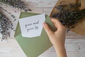 GREEN MIND GREEN LIFE text on supportive message paper note reminder from green envelope. Flat lay composition dry lavender flowers. Concept of eco-friendly lifestyle, environmental recyclable reusable low waste living. Top view photo