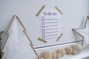 TO DO LIST checklist text on paper note stick on while wall with cozy minimalistic handmade Christmas decor. New year aims resolutions. Low key festive Planning and setting goals concept photo
