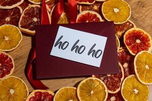 HO HO HO text on postcard with red envelope on dried slices of grapefruit and oranges in Christmas wreath. Zero waste eco-friendly Christmas. Sustainable greeting card decoration photo