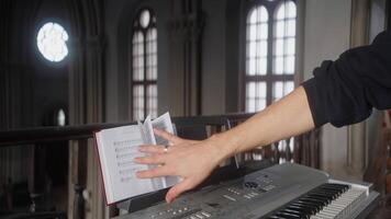 Man with sheet music and piano. Action. Man flips through music book on synthesizer. Close-up of musician on synthesizer in church video