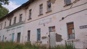 View of an old abandoned house with fallen plaster. Clip. Green grass and old building. video