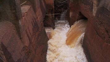 lento movimento do água fluxo do antigo barragem. grampo. sujo córregos do água descer a partir de canal barragem. antigo argila barragem com Gravetos e sujo água video