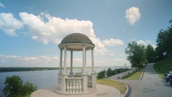 Beautiful landscape with embankment and gazebo in summer. Clip. White gazebo on background of river on sunny summer day. Beautiful white gazebo on river embankment in summer video