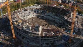 Top view of construction of large stadium in city. Stock footage. Process of building stadium on site with cranes in modern city. Construction of stadium with cranes on sunny day video