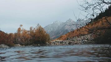 A quick shot of the river in the wind. Creative. Yellow trees with foliage and high mountain hills with walking tourists. video