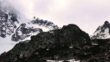 Snow-capped mountain peaks emerging through misty clouds in stunning panorama video
