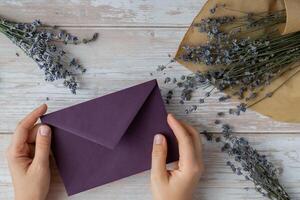Flat lay composition of female hands holding violet envelope with dry lavender flowers. Copy space template mock up. Top view. Concept of Wedding invitation postcard. Business advertisement brand blank photo