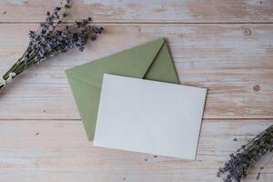 Flat lay composition of white paper greeting card on envelope with dry lavender flowers. Copy space template mock up. Top view. Concept of Wedding invitation postcard. Business advertisement brand blank photo