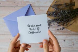 Female hands taking paper card note with text POSITIVE MIND LIFE VIBES from violet envelope. Lavender flower. Top view, flat lay. Concept of mental spiritual health self care wellbeing mindfulness photo