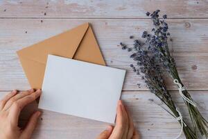 Flat lay composition of white paper greeting card on envelope with dry lavender flowers. Copy space template mock up. Top view. Concept of Wedding invitation postcard. Business advertisement brand blank photo